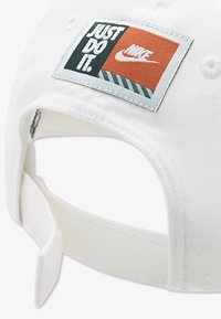 Λευκό καπέλο του μπέιζμπολ με κεντημένο έμπλαστρο σε πράσινο, πορτοκαλί και ανοιχτό μπλε που εμφανίζει το «JUST DO IT» και το λογότυπο της Nike. Ρυθμιζόμενο λουράκι στο πίσω μέρος.