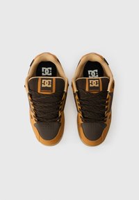 Ténis castanho escuro e areia com um cabedal texturizado, atacadores em contraste com manchas laranja e um logótipo na língua.