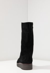Black suede knee-high boot with a smooth texture, rounded toe, and a sturdy rubber sole. Simple design, no visible hardware or accents.