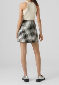 Minifalda con patrón de houndstooth en blanco y negro, combinada con una blusa sin mangas color crema y zapatos de plataforma plateados.