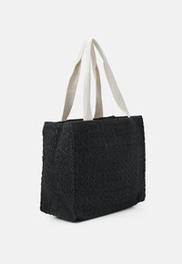 Černá tkaná taška přes rameno s bílými látkovými úchyty, obdélníkový tvar a texturovaný vzor, zobrazená na bílém pozadí.