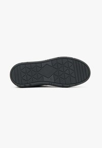 Black rubber shoe sole featuring a textured surface with triangular patterns and a rounded heel. Designed for grip and durability.