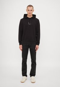 Black hoodie with a drawstring hood and front logo, paired with black pants and white sneakers. Smooth texture, minimalist design.