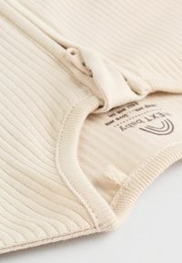 Rippiger beiger Stoff mit rundem Ausschnitt und einem kleinen Etikett. Das Design weist vertikale Streifen und eine weiche Textur auf.