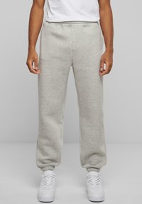 Grå sweatpants lavet af blødt materiale, med en afslappet pasform, elastiske manchetter og sidelommer, parret med hvide sneakers.