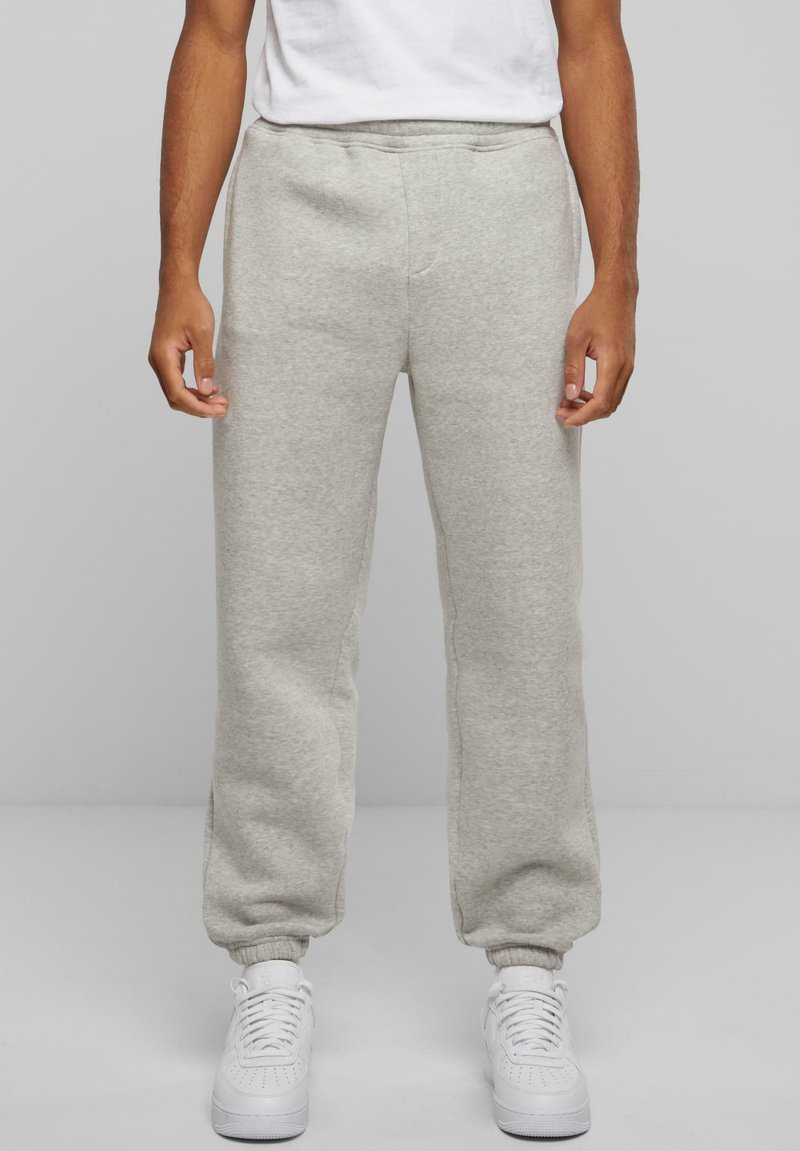 Grå sweatpants lavet af blødt materiale, med en afslappet pasform, elastiske manchetter og sidelommer, parret med hvide sneakers.