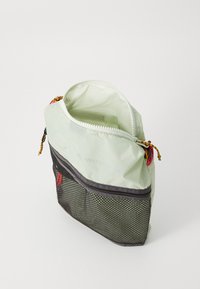 Zöld nylon tasak fekete hálós aljjal, felső cipzáras záródással és színes cipzárhúzóval. Letisztult, téglalap alakú dizájn jellemzi.