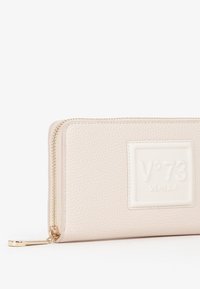 Portafoglio in pelle beige testurizzato con zip dorata, caratterizzato da un etichetta rettangolare goffrata con la scritta "V°73 VENEZIA" sul davanti.