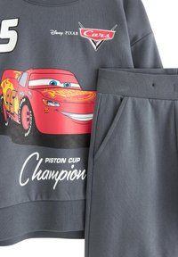 Harmaa collegepaita ja yhdistelemään sopivat housut, joissa on punainen Lightning McQueen -grafiikka ja "Piston Cup Champion" -teksti valkoisella sekä värikkäitä yksityiskohtia.