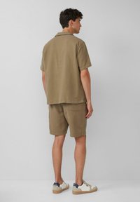 Bruine kortekmouwen shirt en bijpassende shorts van gestructureerd materiaal, met een klassieke kraag en een achterzak op de shorts.