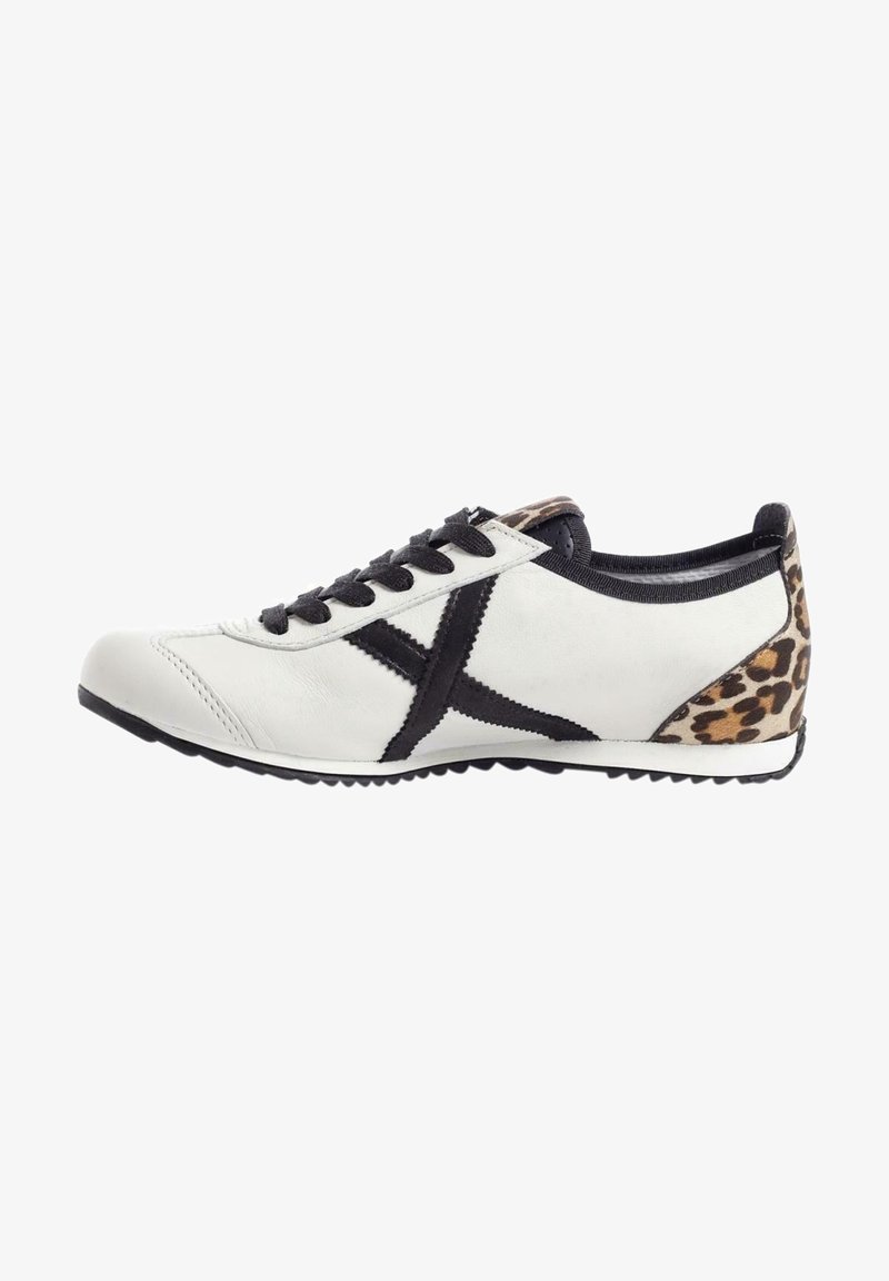 Białe skórzane sneakersy z czarnymi sznurówkami i akcentami. Posiadają panel w leopardzi wzór przy pięcie oraz teksturowaną gumową podeszwę.