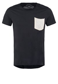 Sort kortærmet t-shirt lavet af bomuld, med en struktureret cremesfarvet lomme på venstre bryst og en buet kant.