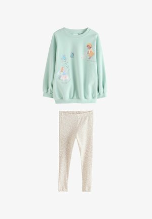 Žalios mėtos spalvos ilgomis rankovėmis megztinis su fėjų ir drugelių iliustracijomis, derinamas su kreminės spalvos tamprais, kuriuose yra nedidelis gėlių raštas.