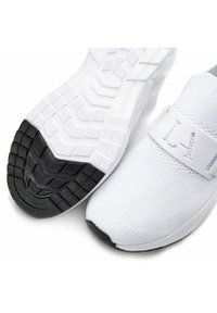 White athletic shoes with a textured knit upper, featuring a wide strap and contrasting black rubber outsole with patterned tread.