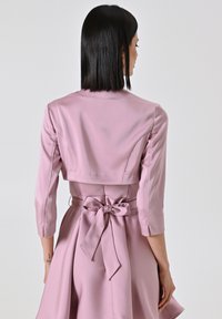 Abito di satin rosa chiaro con maniche a tre quarti, bodice corto e un nastro annodato in vita. Texture liscia e silhouette aderente.