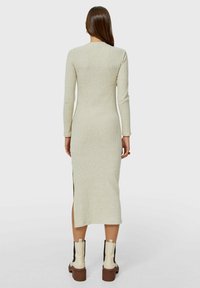 Robe longue à manches longues côtelée en tricot beige clair, d'une longueur mi-mollet avec des fentes sur les côtés. Associée à des bottines crème à plateforme marron.