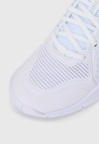 Hvid atletiksko med en tekstureret overdel, mesh-design og en glat sål. Har snørebånd og områder af både faste og åndbare materialer.