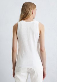 Débardeur blanc sans manches en matériau léger. Présente une coupe décontractée et un col arrondi, vu de dos.