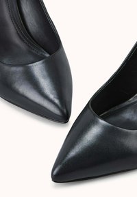 Escarpins noirs en cuir avec un bout pointu, texture lisse et un design de col incliné, présentant un style minimaliste sans embellissements.