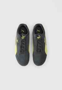 Mustard ja musta värvi Puma tossud, sidemetega, vaated pealt, ühel ühtlasel valgel taustal.