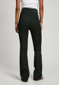 High-waisted black flared jeans made from stretchy material, featuring two back pockets and a subtle logo patch on the waistband.