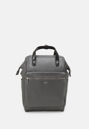 Sac à dos carré gris avec poignées noires, poche avant zippée, poches latérales et tirette de fermeture éclair argentée, présenté sur fond blanc.