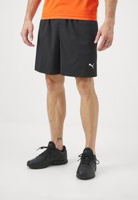 Melni sporta šorti ar gludu tekstūru un elastīgu jostu, ar mazu balto Puma logo. Apvienoti ar melniem čības.