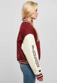 Maroon varsity jacket with cream sleeves, ribbed collar, and "FUBU" lettering on the left arm. Soft fabric and sporty design.