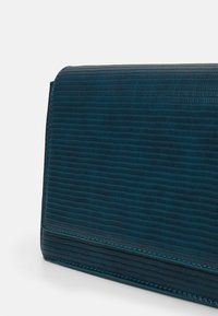 Teksturowana turkusowa kopertówka o strukturalnym wzorze, z gładką powierzchnią i kontrastującym przeszyciem. Zapięcie jest dyskretne.