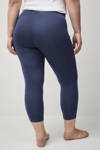 Marineblauwe capri-legging met een gladde textuur, middelhoge taille en een aansluitend ontwerp, gecombineerd met blote voeten en een eenvoudig topje.