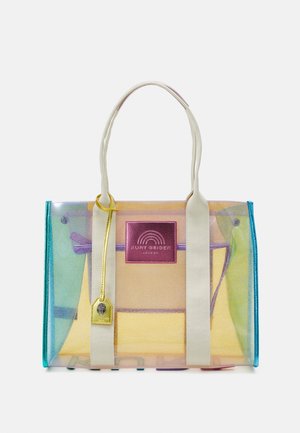 Bolsa tote transparente con asas blancas, bolsa interior morada, bordes azul verdoso, parche de logo rosa y etiqueta colgante amarilla.