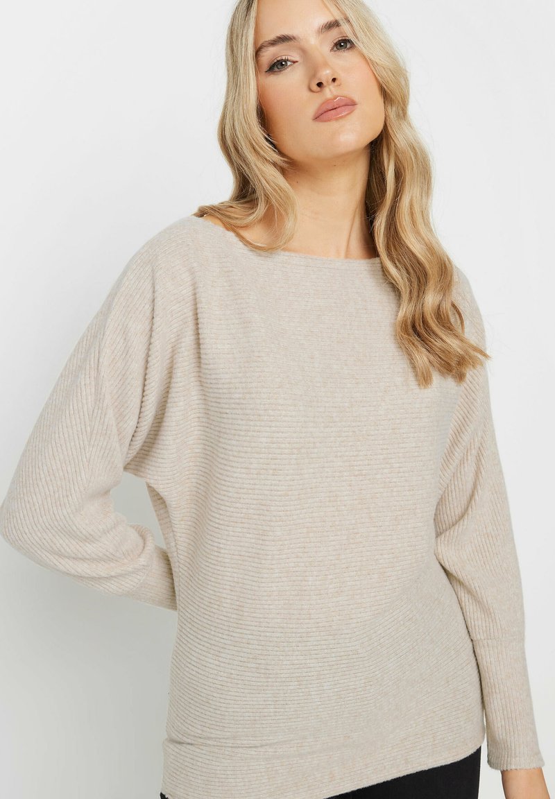 Beige ribbknitted neulepaita, jossa on leveä kaula-aukko ja roikkuva olkamuoto. Pehmeä rakenne ja hienovaraiset pystysuorat raidat. Rennon istuvuuden.