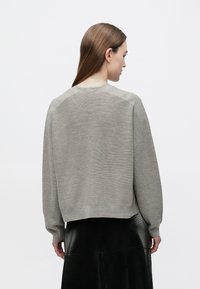 Maglione grigio lavorato a maglia con texture a coste, scollo arrotondato e design a spalle scese, indossato sopra una gonna nera con texture.