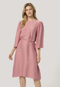 Rosa midiklänning med en texturerad tyg, rund halsringning och ärmlängd vid armbågen. Har ett bälte i midjan för justerbar passform.