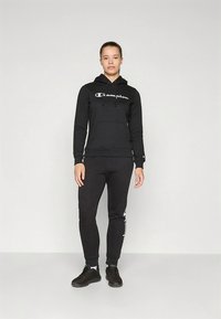 Ensemble sweat à capuche noir et pantalon de survêtement en mélange de coton. Le sweat à capuche comprend une poche avant et un cordon de serrage, avec un logo blanc sur la poitrine.
