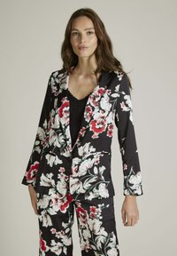 Blazer à imprimé floral noir, comportant des fleurs blanches et rouges. Design ajusté avec revers, fermeture à bouton et deux poches avant.