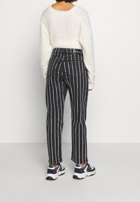 Svartvita randiga jeans med hög midja och tryckta detaljer. Kombinerat med en mysig vit stickad tröja och sportiga sneakers.