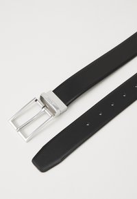 Ceinture en cuir noire avec une boucle rectangulaire en argent, bords proprement finis, plusieurs trous pour l'ajustement et une texture lisse.