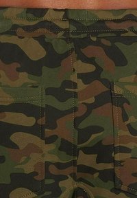 Pantaloni corti mimetici in diverse tonalità di verde e marrone. Presenta due tasche posteriori e dettagli di cucitura visibili. Tessuto in cotone.