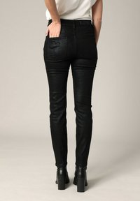 Jean en faux cuir noir avec une texture serpent, design près du corps, cinq poches et une coupe droite, associés à des bottes noires à talons.