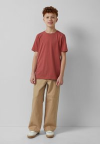 Rode katoen T-shirt met korte mouwen, gecombineerd met beige wijde pijpenbroek en witte sneakers met bruine zolen. Eenvoudige en casual outfit.