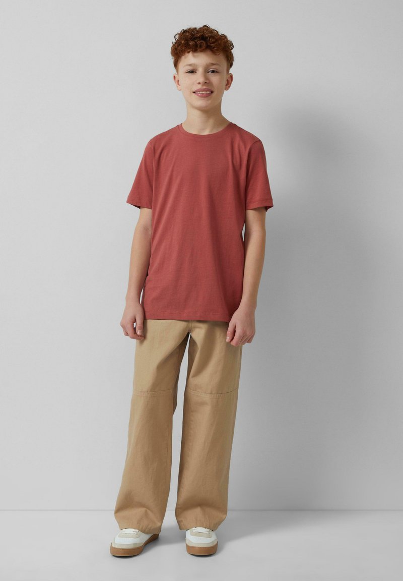 Rode katoen T-shirt met korte mouwen, gecombineerd met beige wijde pijpenbroek en witte sneakers met bruine zolen. Eenvoudige en casual outfit.