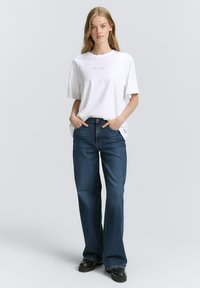 T-shirt bianca in cotone con maniche corte e piccole scritte, abbinata a jeans in denim blu a gamba dritta e scarpe con platform nere.