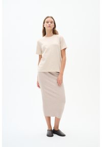 Beige pletené tričko a outfit s řasenou sukní. Tričko má krátké rukávy a kulatý výstřih; sukně je dlouhá po kotníky. Dark slip-on boty.
