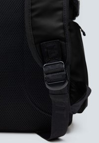 Mochila negra con un panel de malla texturizada, correa ajustable con un cierre de plástico seguro y acentos de tela suave.