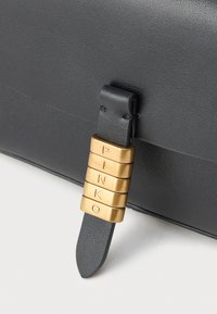 Sort tekstureret lædertaske med et guldfarvet hardware-akkord med indgraverede bogstaver, der staver "PINKO", samt en glat stroppenedetail.