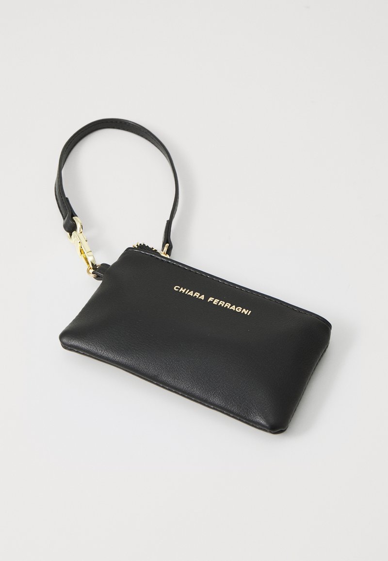 Pochette en cuir noir avec une fermeture éclair et des accessoires dorés. Présente un logo doré en relief à l'avant. Texture lisse et forme rectangulaire.