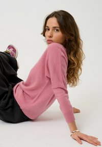 Suéter de cachemira rosa con mangas largas y puños acanalados, combinado con pantalones negros y zapatillas, que presenta una superficie texturizada y un corte relajado.
