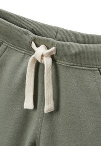 Un pantalon de survêtement en coton vert avec une taille côtelée dotée d'un cordon blanc noué, et une surface lisse et texturée.