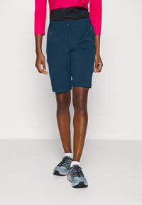 Marineblauwe wandelschoenen met een aansluitende stijl, twee met rits afgesloten zakken en opgerolde zomen, gecombineerd met grijze en zwarte sportschoenen.